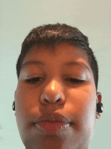 a young boy wearing earbuds looks at the camera with his eyes closed