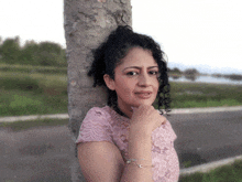 a woman with curly hair leans against a concrete pole