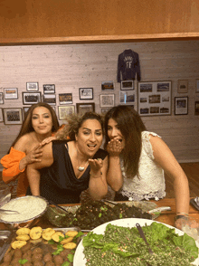 three women are sitting at a table with plates of food and a shirt that says ff