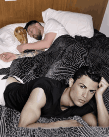 a man in a black shirt is laying on a bed next to another man