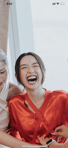 a woman in a red robe is laughing while another woman holds her