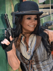 a woman in a bowler hat is holding a gun and smiling