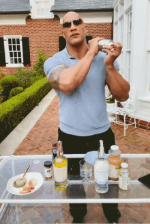 a man in a blue shirt is shaking a drink in front of a table with bottles of alcohol and a plate of food on it