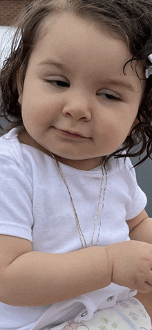 a baby girl wearing a white shirt and a gold chain