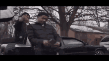 a man is standing next to another man in front of a car .