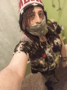 a woman is taking a selfie in a bathroom while wearing a mask and a hat .