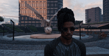 a man with dreadlocks and sunglasses stands in front of a statue