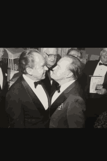 a black and white photo of two men in tuxedos kissing