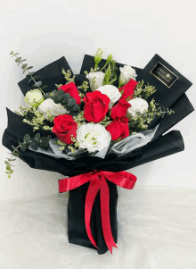 a bouquet of red and white roses wrapped in black paper with a red ribbon