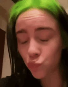 a woman with green hair is making a face with her eyes closed .