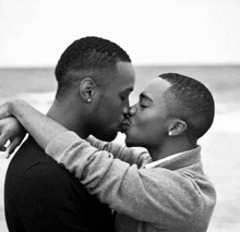 two men kissing on a beach with the ocean in the background