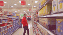 a man in a red jacket is walking down a grocery store aisle with a sign that says quaker on it