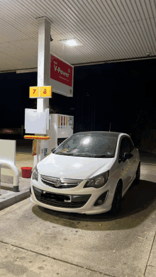 a white car is parked in front of a shell v-power gas pump