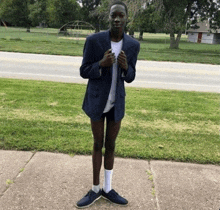 a young man wearing a suit jacket and shorts stands on a sidewalk