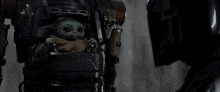 a baby yoda is sitting in a robot 's stroller .