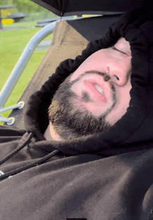 a man with a beard wearing a black hoodie is sleeping in a chair