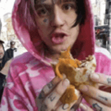 a man in a pink hoodie is holding a sandwich in his hands .