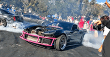 a black sports car with a pink bumper is drifting on a dirt road .