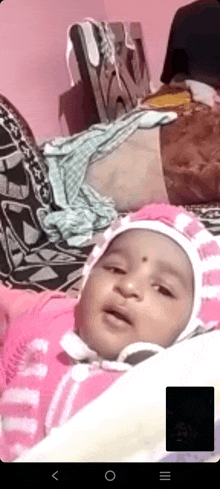 a baby is laying on a bed with a pink and white striped hat on .