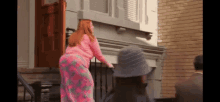 a woman in a pink shirt and pink pants is standing on the steps of a house .