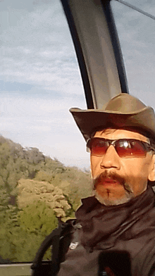 a man wearing a cowboy hat and sunglasses is sitting in a car