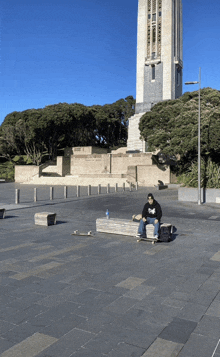 a man sits on a bench with a skateboard and a bottle of water in front of a building