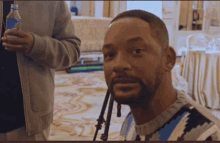 a man with a beard looks at the camera while a man holds a bottle of aquafina water in his hand