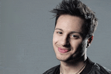 a young man wearing a black jacket and necklace is smiling