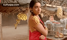 a woman in a red sari is standing in front of a table with bananas hanging from the ceiling .