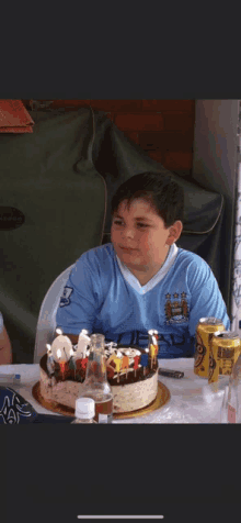 a boy wearing a shirt that says ' manchester city ' on it sits at a table with a birthday cake