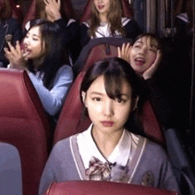 a group of girls are sitting in red chairs on a bus .