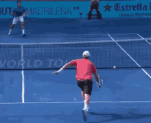 a man in a red shirt is playing tennis on a blue court with an estrella advertisement in the background