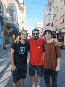 a man wearing a red shirt that says lacoste poses with two other men