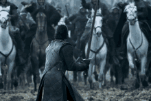 a man holding a sword stands in front of a crowd of men on horses