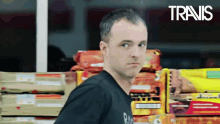 a man in a black shirt is standing in front of a stack of fireworks and a sign that says travis