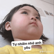 a baby is wearing a yellow shirt and has a sticker on her face that says " tự nhiên nhớ anh yêu