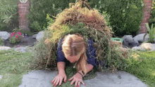 a woman is crawling under a pile of grass with a sign in the background that says ' a '