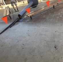 a broken pipe is sitting on the ground next to a wooden bench with orange flags .