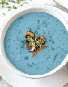 a bowl of blue soup with mushrooms on top on a plate .