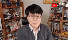 a man wearing glasses is sitting in a chair in front of a bookshelf filled with books .