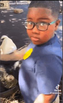 a young boy wearing glasses and a blue shirt is standing next to a trash can .