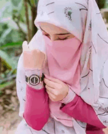 a woman wearing a hijab and a watch is holding her watch .