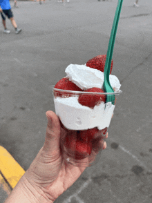 a person holds a cup of strawberries and whipped cream