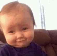 a baby is sitting on a couch smiling at the camera .