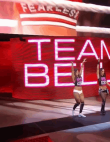 two women are walking on a stage in front of a large screen that says team bell