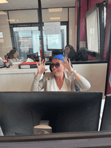 a woman wearing sunglasses and a blue headband is sitting in front of a computer monitor