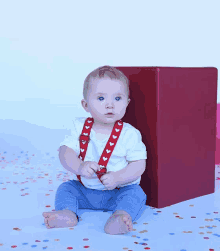 a baby wearing red suspenders with white hearts