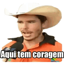 a man wearing a cowboy hat is talking into a microphone and saying aqui tem coragem .