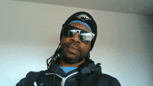 a man with dreadlocks wearing sunglasses and a beanie with a shark logo on it