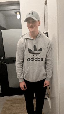 a man wearing a grey adidas hoodie and a hat